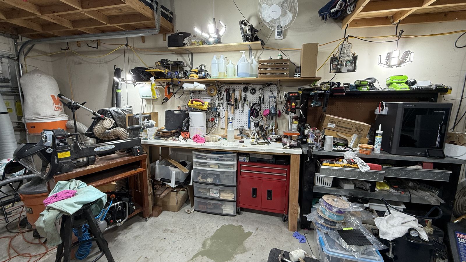 Jen's garage wood workshop: her lathe, WEN dust collector, a workbench with a pegboard of turning tools and safety gear, her WEN drill press and LED garage lights overhead